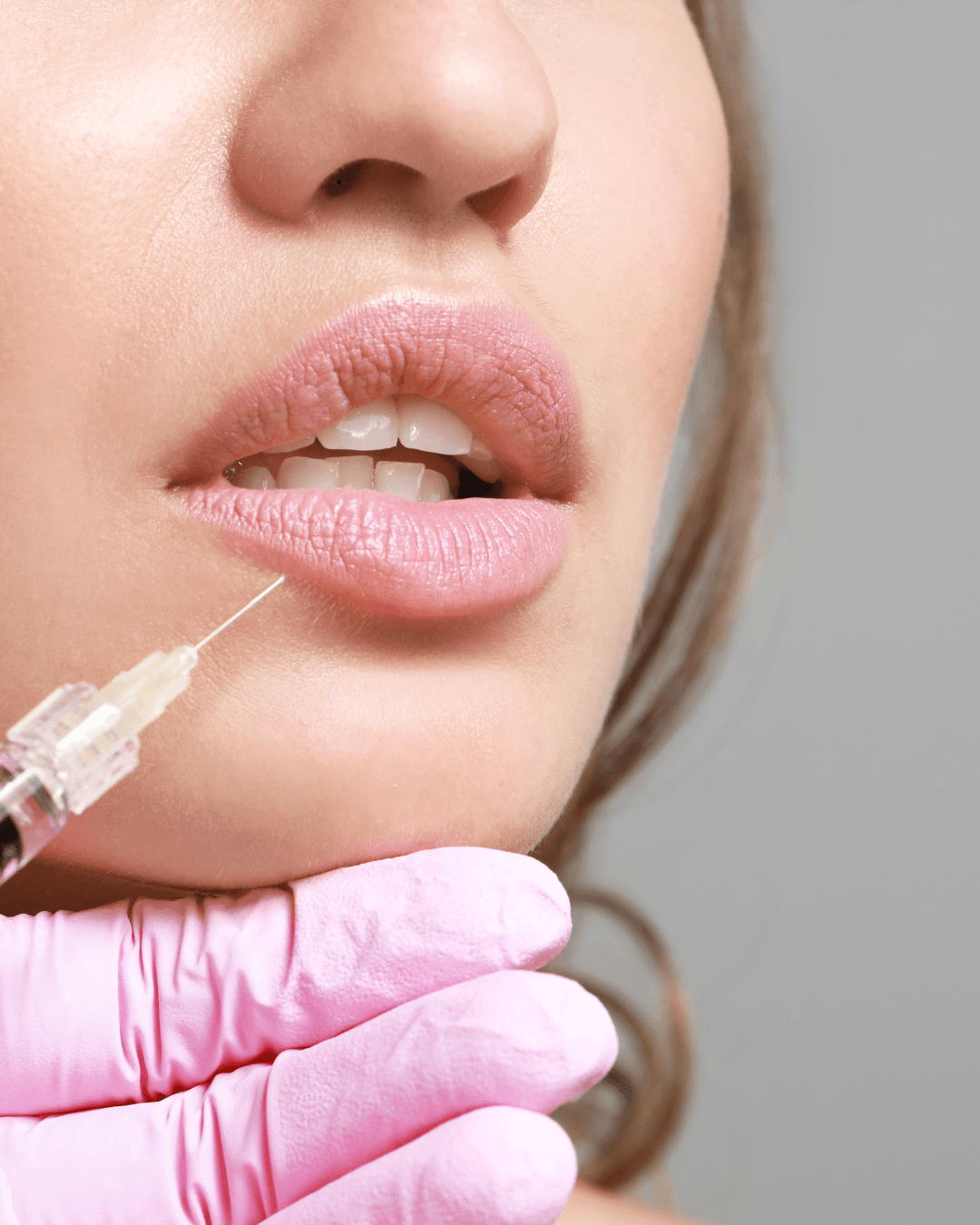 Close-up of a woman receiving a cosmetic injection into her lower lip from gloved hands.